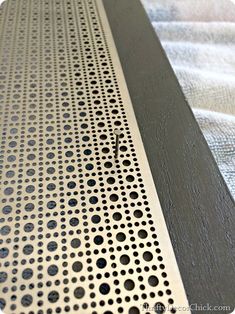 a metal grate with holes on it sitting on a sheet of white fabric next to a bed