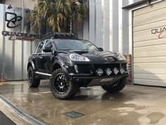 a black suv parked in front of a garage door with palm trees on the side