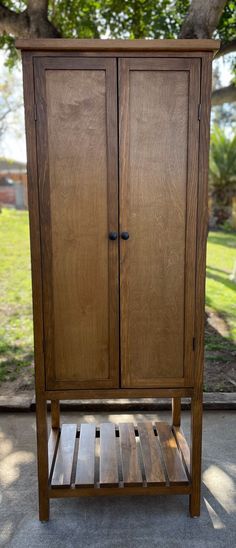 a wooden armoire sitting on top of a sidewalk next to a tree and grass