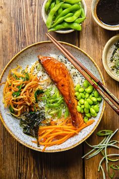 a bowl filled with fish and vegetables next to chopsticks on top of a wooden table