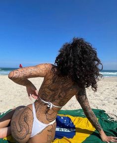 a woman sitting on top of a beach covered in tattoos