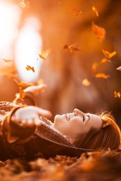 a woman laying on the ground with her eyes closed and falling leaves in the air