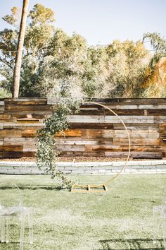 an outdoor ceremony setup with white chairs and greenery on the grass in front of a wooden wall