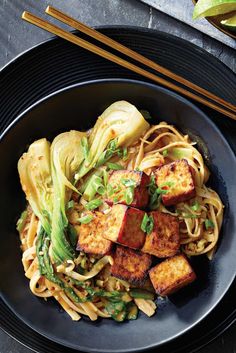 a black plate topped with noodles and tofu