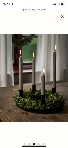 four candles sitting on top of a wooden table with greenery around the candle holders