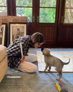 a woman kneeling on the floor playing with a kitten