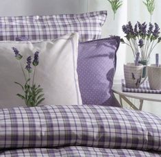 a bed with purple and white plaid sheets, pillows and vases on the side table