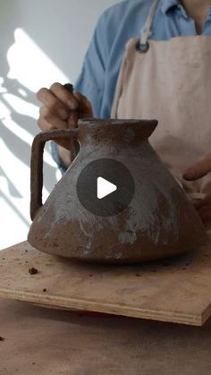 a man is making a clay pot on a wooden table with an apron over his shoulder