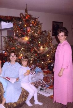 an old photo of three women and a child in front of a christmas tree with presents