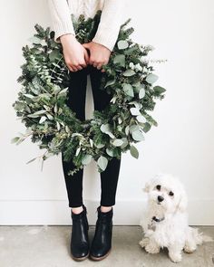 a woman standing next to a white dog with a wreath on it's face