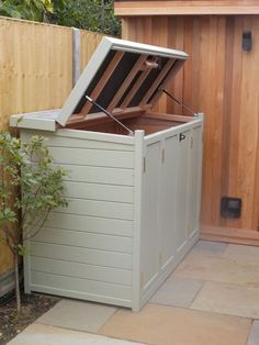 an outdoor storage box with the lid open in front of a wooden fenced area