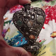 a person is holding an ornate silver heart shaped object with stones in it's center