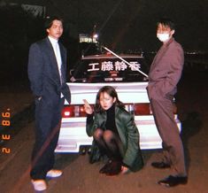 two men and a woman standing next to a car