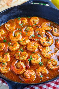 a skillet filled with shrimp and sauce on top of a checkered table cloth