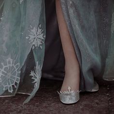 a woman's feet wearing silver shoes with snowflakes on them and sheer fabric