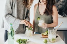 two women standing at a table with drinks and limes in front of the woman