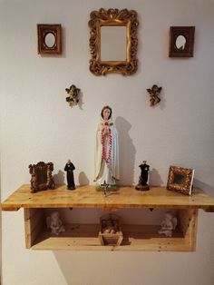 a wooden shelf with figurines on it in front of a white wall and framed pictures