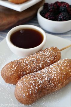 two dessert sticks on a plate with berries and dipping sauce