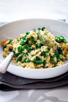 a white bowl filled with macaroni and cheese covered in green vegetables next to a spoon