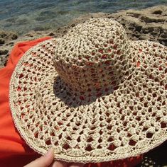 a person is sitting on the beach with a hat in their hand and there is water behind them