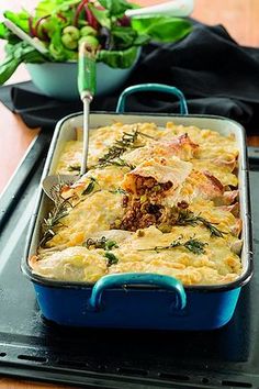 a casserole dish with meat and vegetables in it on a tray next to a salad