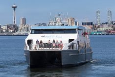 a ferry boat with passengers on the deck in front of a cityscape and water