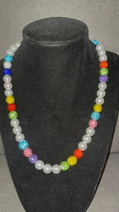 Grab this customRainbow color themed Baseball Pearl beaded necklace with pops of color throughout.  Red Green Yellow Blue Rhinestone Beads Wear it just like the pros! 20 inch w/ magnetic clasp for ease and comfort. (request for longer/shorter) Elevate your style AND your game with our vibrant, handcrafted beaded necklace.   🌟 Features: 🌟 Unique Design 💎 Quality Matters: Thick Elastic band and screw clasp ensure durability and long-lasting wear. 🌟 Versatile Wear: Perfect for all sports fields😎, beach days, date nights, or simply adding a pop of personality to your everyday look. A conversation piece. 📸 Instagram-Ready: Be prepared for compliments and photo ops wherever you go! Follow DingerCityDrip on IG Black Silver White Cross Beaded Necklace Fruit Loop Phillies Yellow Orange Green White Bling Round Beads Jewelry, Bling Round Beads Necklace For Gift, Gift Necklaces With Bling And Round Beads, Gift Bling Round Beads Necklaces, Gift Round Beads Bling Necklace, White Necklaces With Colorful Beads For Birthday, Colorful Round Beads Necklace For Birthday, Gift Rhinestone Beaded Necklaces, Multicolor Round Beads Jewelry With Rhinestones