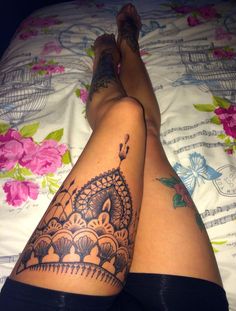 a woman laying on top of a bed with her legs crossed and tattoos on her leg