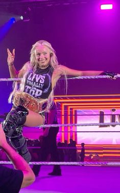 a woman in a wrestling ring with her hands up and one leg on the ropes