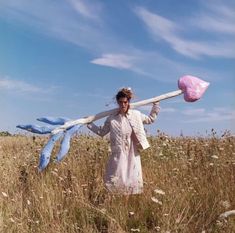 a woman in a field holding a pink and white scarf over her shoulder with two blue ribbons on it