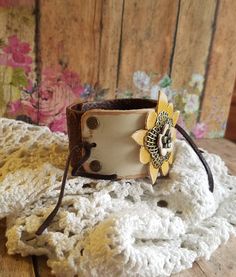 "RUSTIC in style yet so utterly FEMININE ❤ One of my FAVS! ❤ A sweet triple layer flower comprised of leather and metal filigree was painted in shades of yellow and ivory. A tiny bronze flower sits center. ❤ The ivory leather was hand-painted and tied with chocolate brown deerskin lacing to rustic brown tooled leather. ❤ Rivets add dimension and hold it securely on the cuff. ❤ The width of the cuff is approximately 1 1/2\" wide. BRACELET SIZING INFO: My women's bracelets are approximately 8 1/2 Handmade Bohemian Flower Cuff Bracelet, Bohemian Flower Cuff Bracelet Handmade, Adjustable White Leather Bracelet, Adjustable Bohemian Flower Cuff Bracelet, Bohemian Flower Cuff Bracelet As A Gift, Bohemian Flower Cuff Bracelet As Gift, Bohemian Adjustable Flower Cuff Bracelet, Bohemian Flower Cuff Bracelet, White Leather Bohemian Jewelry