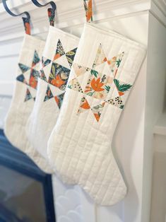 three quilted christmas stockings hanging from hooks on a fireplace mantel, decorated with orange and green flowers