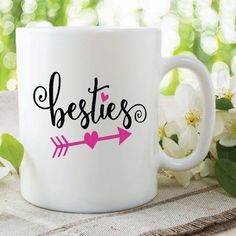 a white coffee mug with the words besties and an arrow on it next to flowers