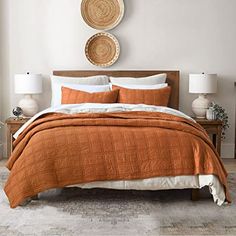 a bed with an orange bedspread and two baskets on the wall above it