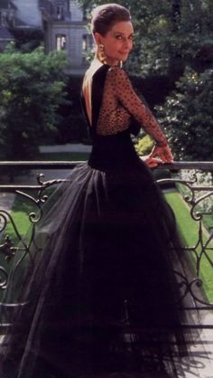 a woman in a black dress standing on a balcony