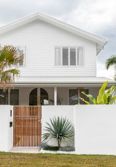 a white house with a wooden gate and palm trees in the front yard, on a cloudy day