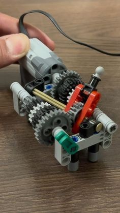 a hand holding a lego robot on top of a wooden table next to a wire