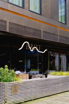 an outside view of a restaurant with plants in the foreground and large windows behind it