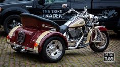 two motorcycles parked next to each other in front of a black truck with the words the trike trader on it's side