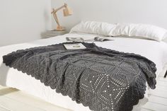 a white bed topped with a black blanket and pillows next to a night stand on top of a wooden floor