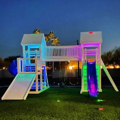 an illuminated play set with slide and slides in the grass at night, lit up by colorful lights