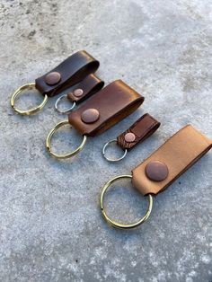 three leather key fobs with brass rings and brown leather handles on concrete surface