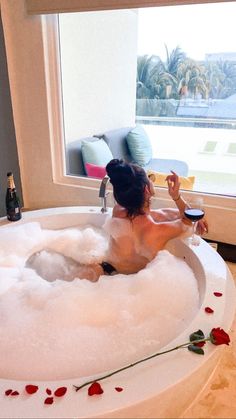 a woman sitting in a bathtub with rose petals on the floor next to a window