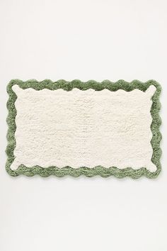 a green and white rug with scalloped edges on a white surface, in the shape of a rectangle