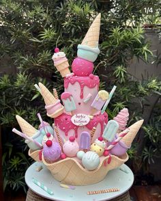 an ice cream cone cake with pink icing and lots of sweets on top is sitting on a table