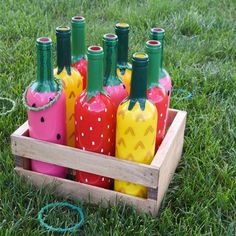 a wooden crate filled with lots of colorful painted bottles in the middle of some grass