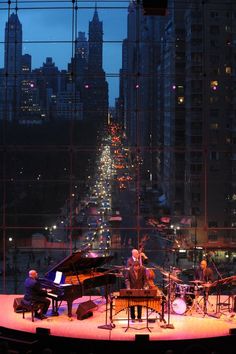 a group of people playing instruments on stage in front of a cityscape at night