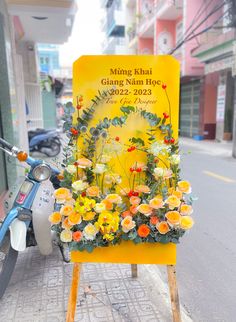 a yellow sign with flowers on it sitting next to a scooter