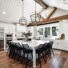 a large kitchen with white cabinets and wooden floors, an island table surrounded by black chairs