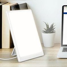 an open laptop computer sitting on top of a wooden desk next to a white plant